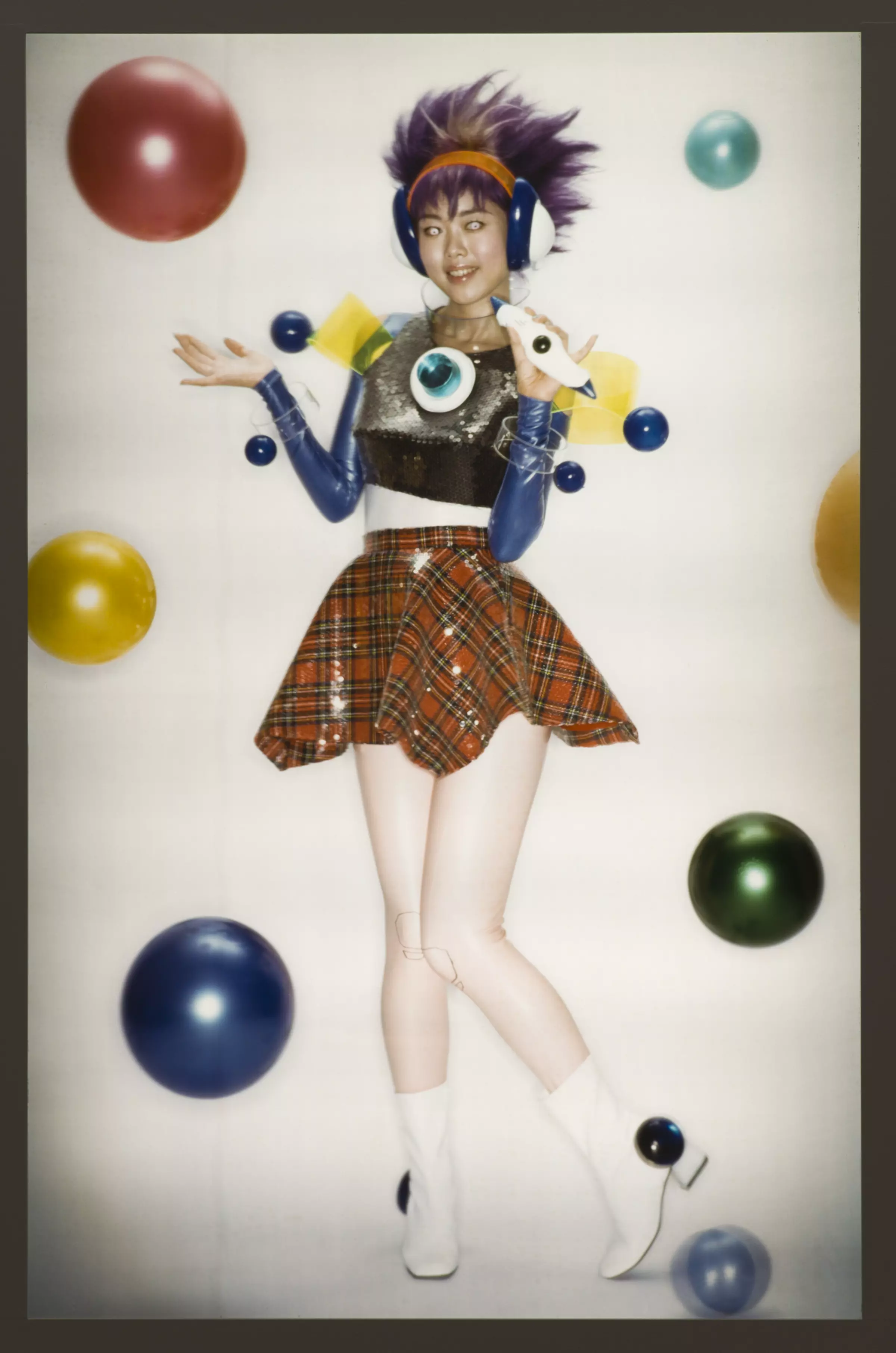 Poppy photograph of a person in a plaid skirt with purple hair and headphones surrounded by different colored circular objects