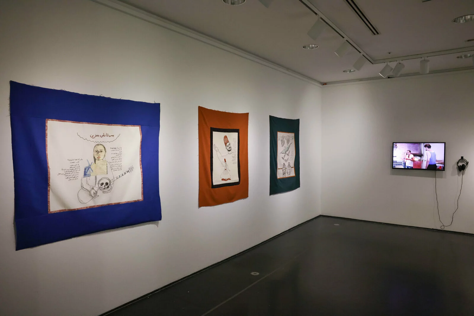 A corner of a dim gallery space with three works on the left wall; a video artwork is just visible on the right.