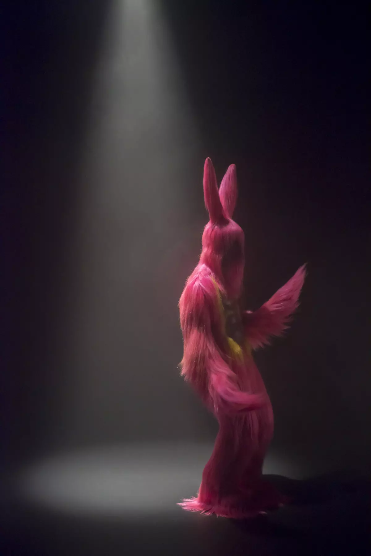A performer on a dark hazy stage wears a shaggy pink costume resembling a bunny
