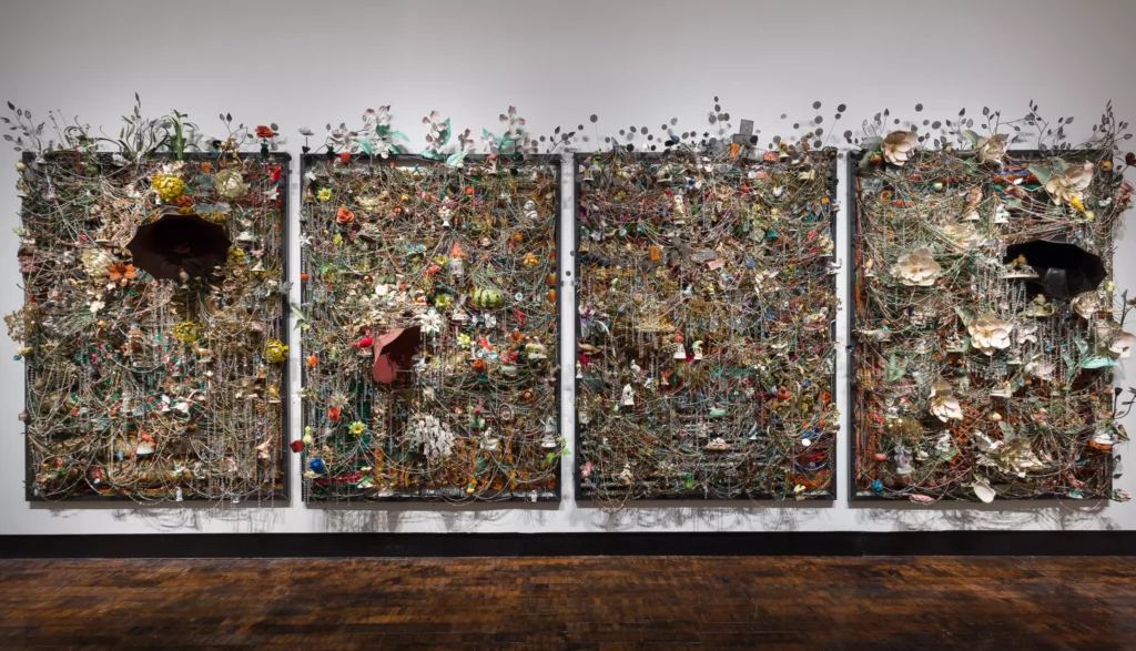 Four panels on a wall each contain a collage of ceramic birds, metal flowers, afghans, strung beads, and crystals; two contain antique gramophones.