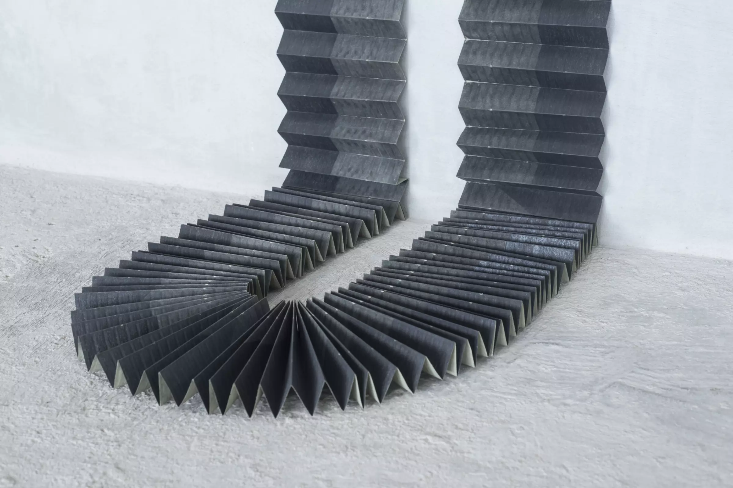 accordion-like folded paper runs down gallery wall, u-turning at the floor as it runs back up