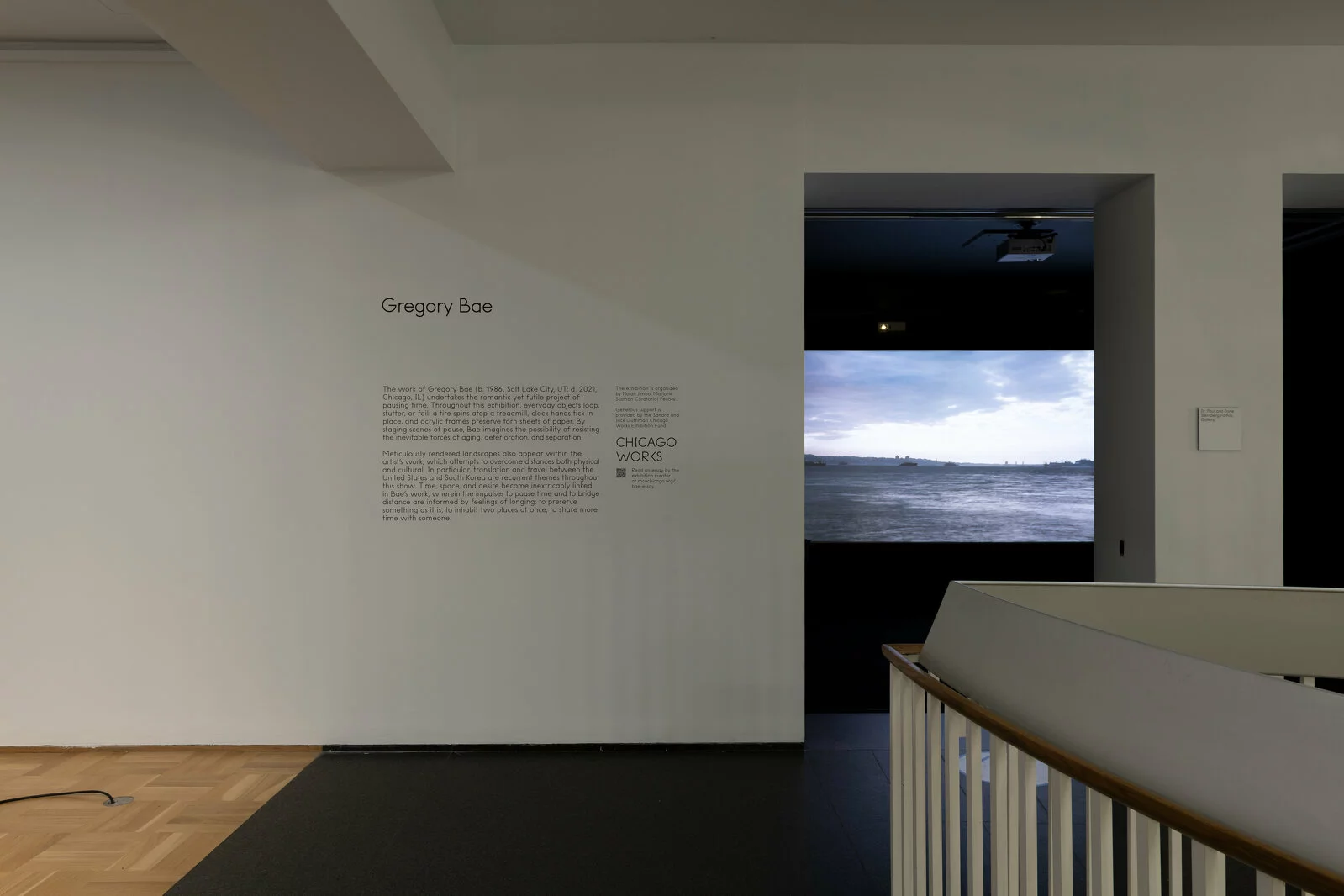Gallery space with open doorway leading into darkened room with video artwork partially seen.
