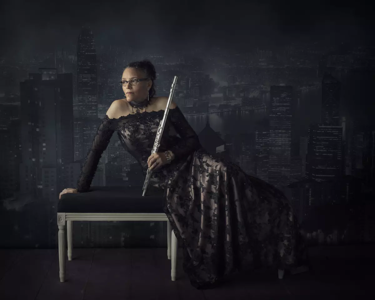 portrait of Nicole Mitchell in a black, long-sleeved gown sitting on a bench holding a flute against a dark background