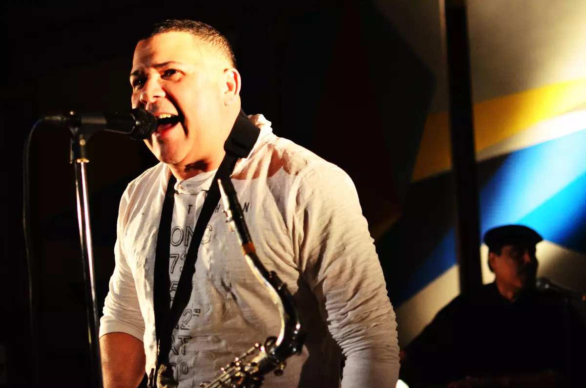 Papo Santiago pauses from playing saxophone to sing into microphone