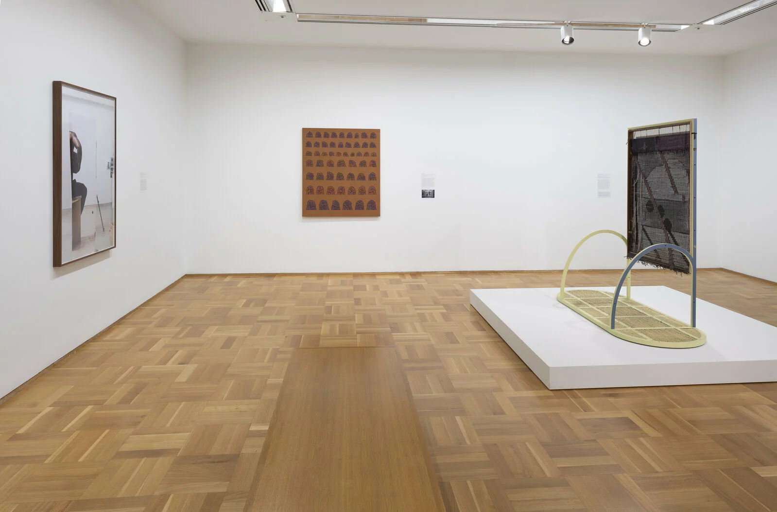 Three artworks on display in a white-walled gallery space. Two hang on the wall; one is installed on a pedestal.