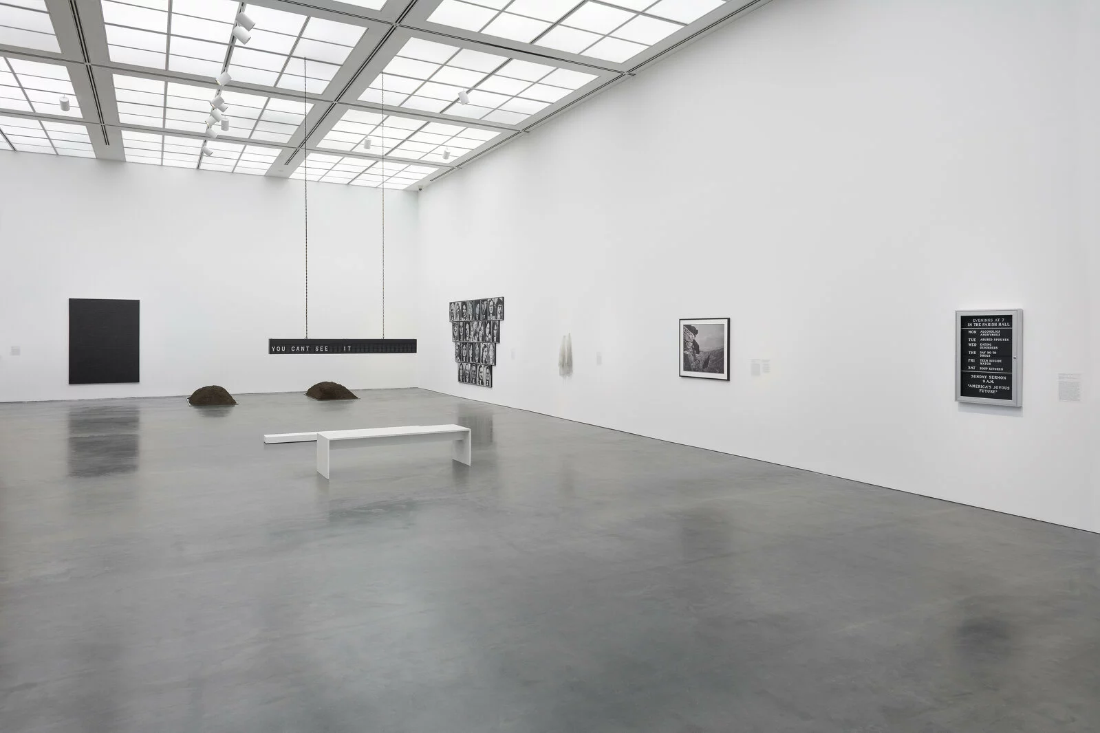 Large, white gallery space with five artworks visible. Three are hung on the wall; two are installations.