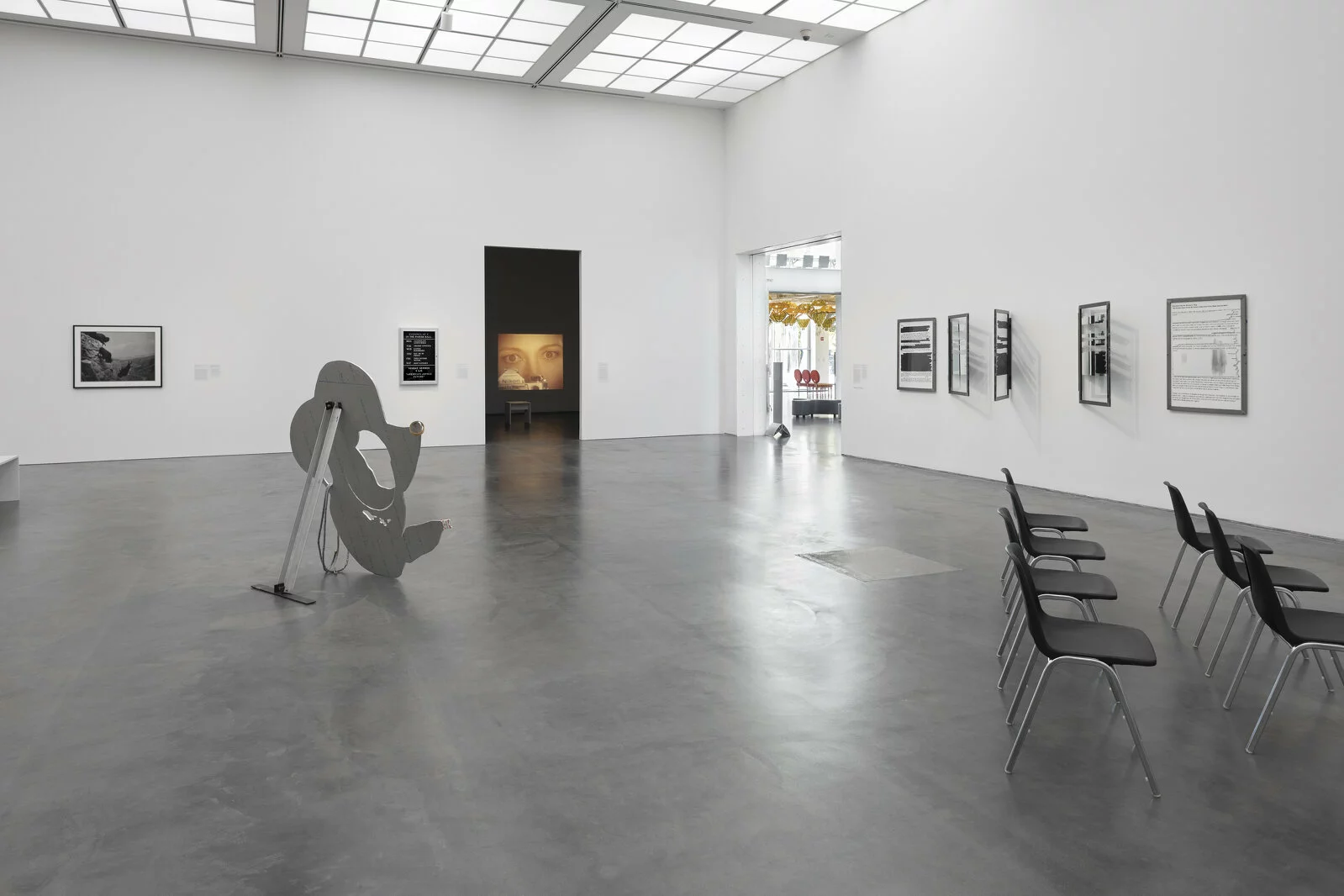 A large, white-walled gallery space filled with several artworks visible. It opens to two doorways, through which you can see additional artworks.