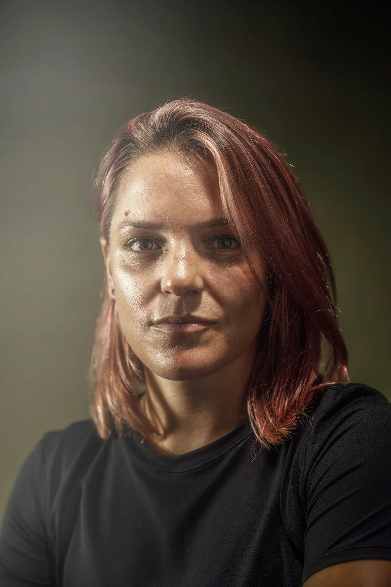 Slightly hazy portrait of a woman with medium-length pink hair and an eyebrow piercing in a black shirt.