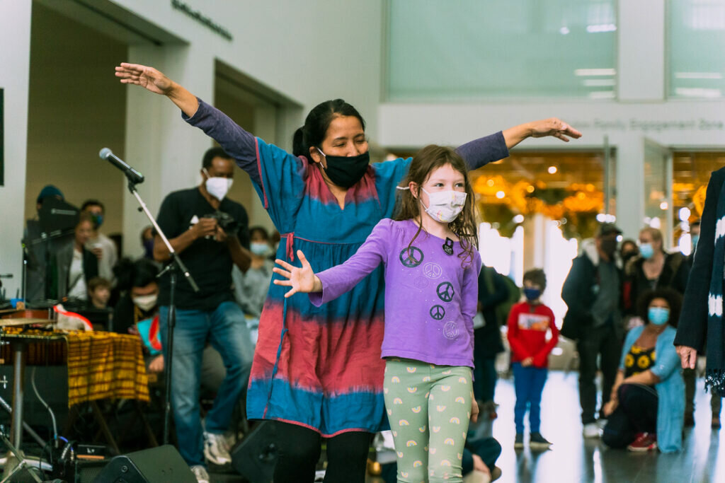 A woman and young girl dance in the MCA Commons surrounded by instruments and a crowd of people.