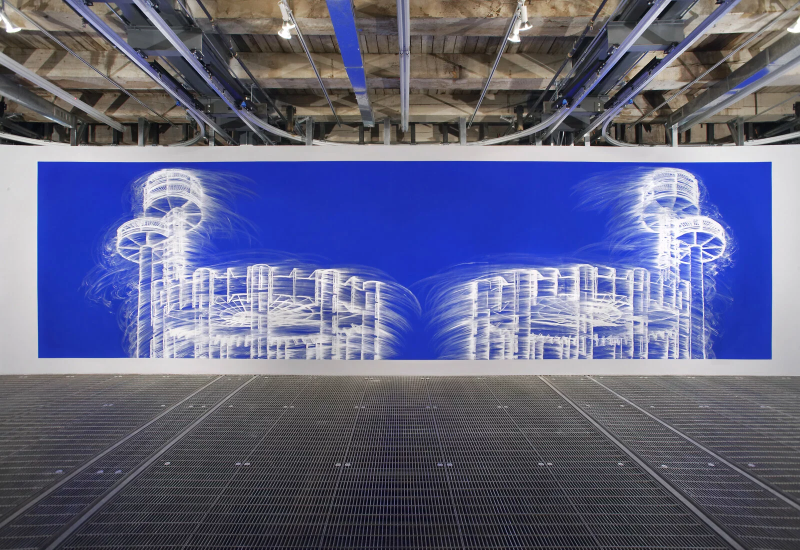 A wide blue artwork with a smeared white line drawing hangs on a white wall in an industrial-type room.