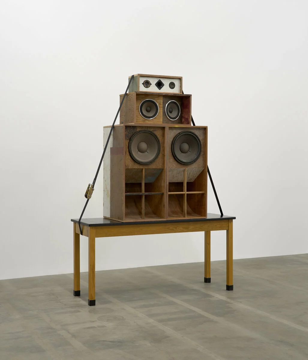A top a wooden table are four different sound system speakers held down by straps.