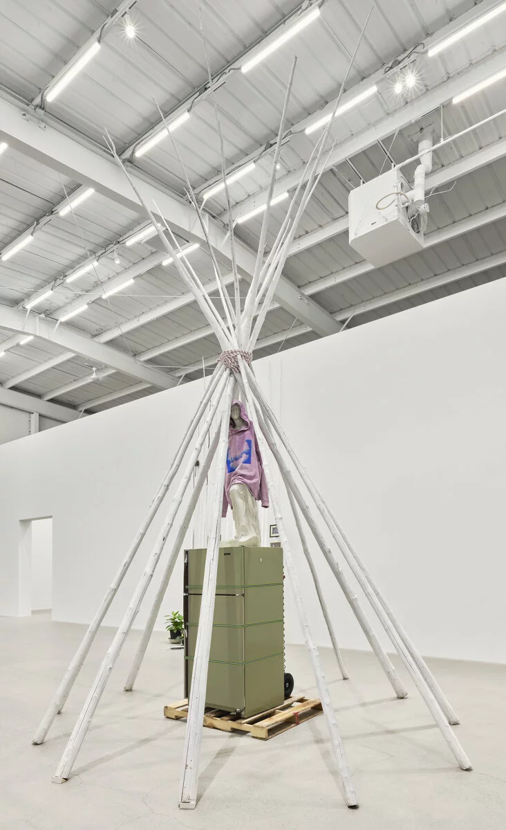 Duane Linklater, what grief conjures, 2020. Teepee poles, paint, nylon rope, wooden pallet, refrigerator, tie-down straps, hand truck, plastic statue, handmade hoodie, cochineal dye, silkscreen. 249 × 160 × 160 in. (633 × 406 × 406 cm). Courtesy Catriona Jeffries, Vancouver. Photo: Rachel Topham Photography. 2022/12/Linklater_what-grief-conjures_2020_primaryuse_CJ_2020_01.jpg 