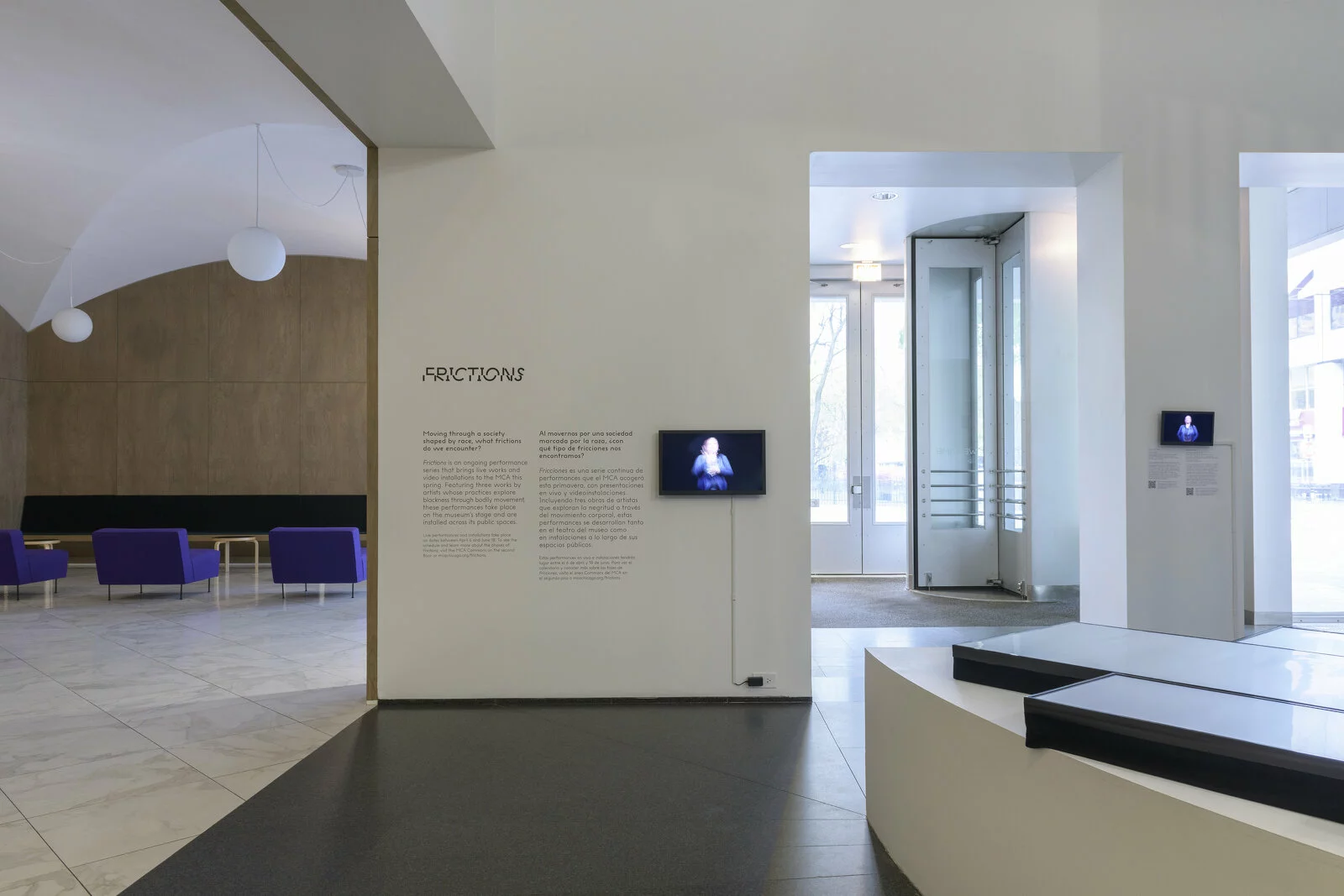 View of exhibition text next to a small video screen on a white wall.