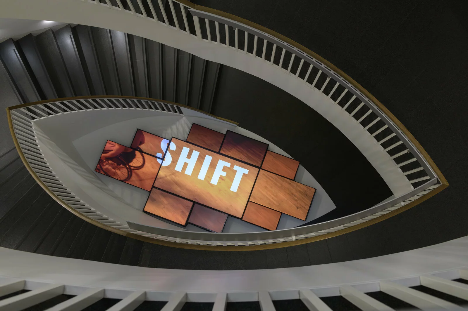 View from the MCA staircase looking down on ten screens in a tight arrangement that together display the word Shift against a peach background.