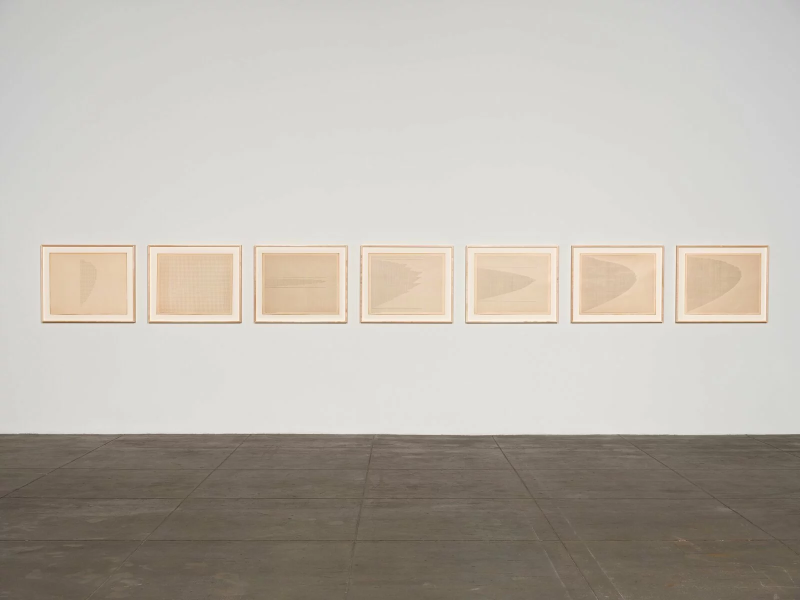 Photo of 7 framed pieces of paper with ink, hung horizontally.