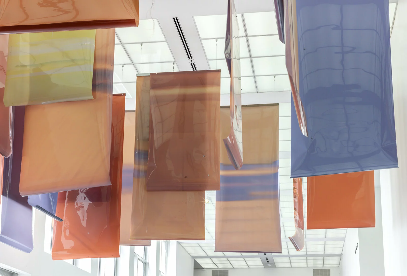Large pieces of blue, orange, peach, and yellow plastic hang from the ceiling of a large, white space.