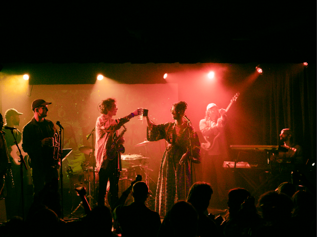 Photo of a live music performance with five people backlit with red and yellow.