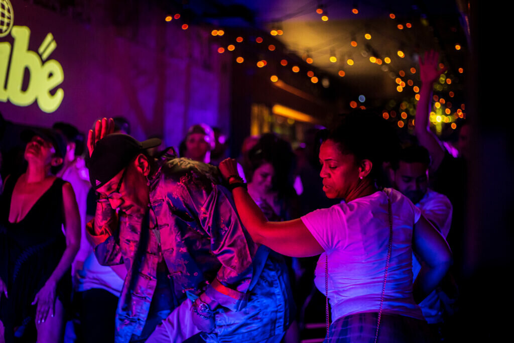 A group of people dance in a purple-lit room with red twinkle lights on the ceiling.
