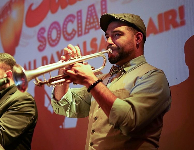 A light skinned person of color blows into a trumpet.