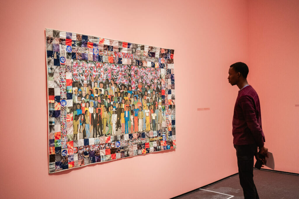 A person stands alone in a gallery painted pink, examining a work hung on the wall.