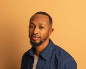 Portrait of a Black man with a slight beard against a light orange wall.