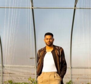 Portrait of a Black man standing within a steel hoop greenhouse system. 
