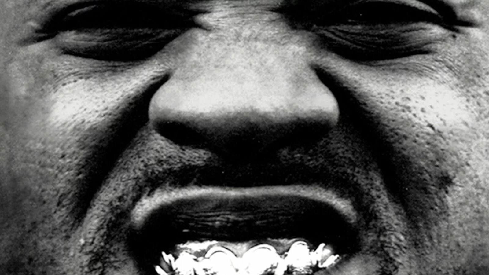 Still black and white shot of a black person scrunching up their nose to display a grill on their teeth.