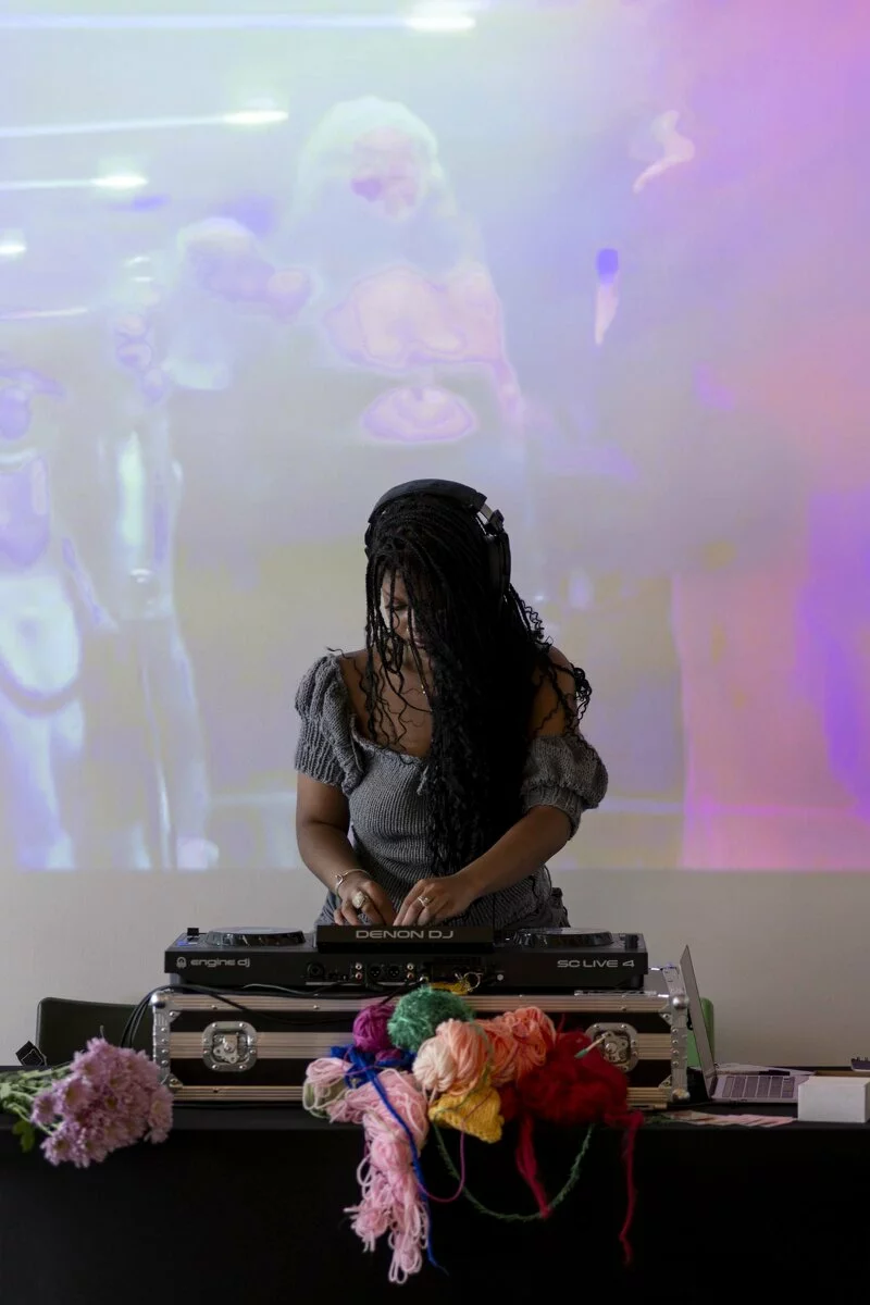 A young Black DJ performs in front of a screen.