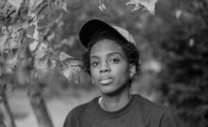 Black-and-white portrait of a  Black woman with short hair among foliage.