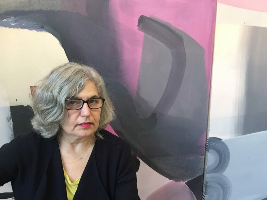 A woman with a gray bob poses in front of a large abstract painting