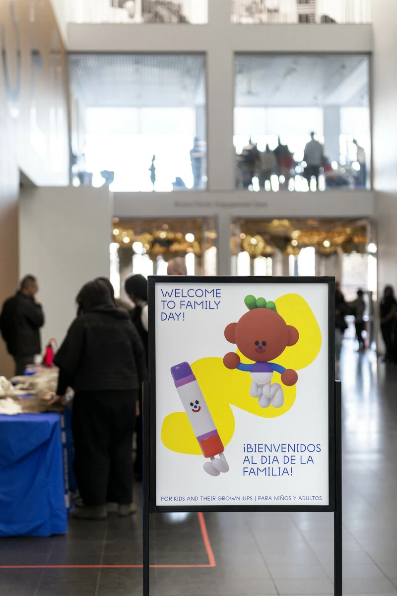 Image of a Family Day sign at the MCA with people at a signup table in the background.