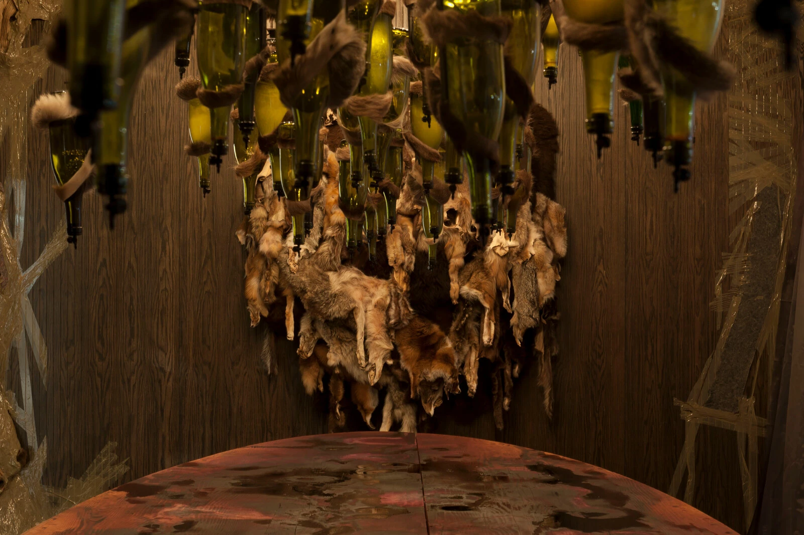 A wood-clad room filled with hanging animal pelts and corked wine bottles over a table.