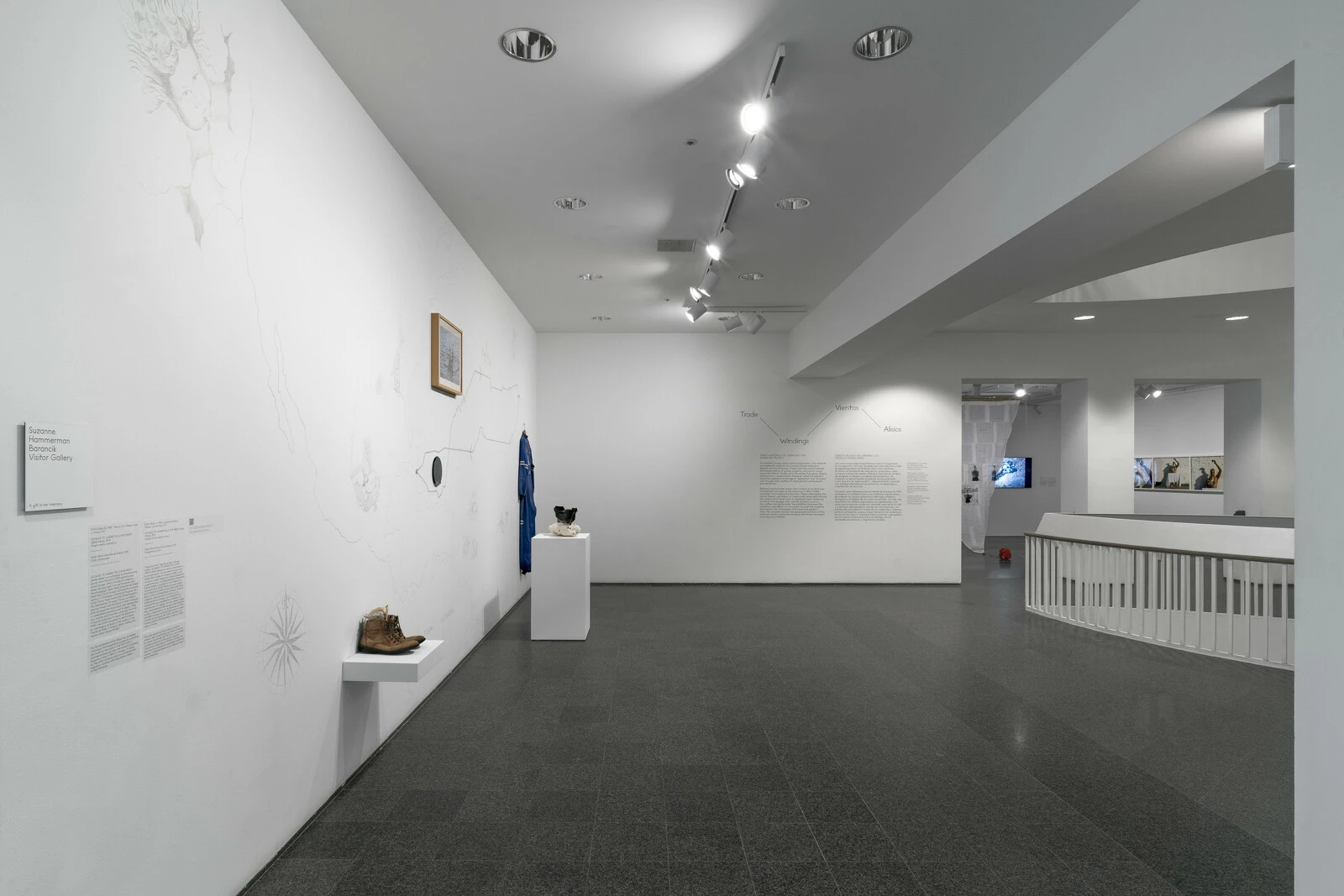 An open gallery space with several objects on the left wall. In the background two doorways lead to another room filled with artworks.