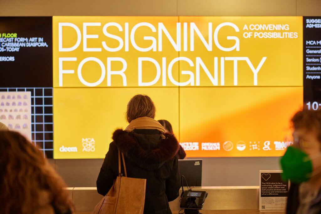 A person stands in front of a digital sign that reads DESIGNING FOR DIGNITY.