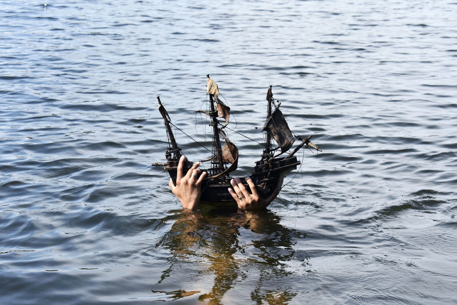 Hands hold a wooden toy ship out of the water.