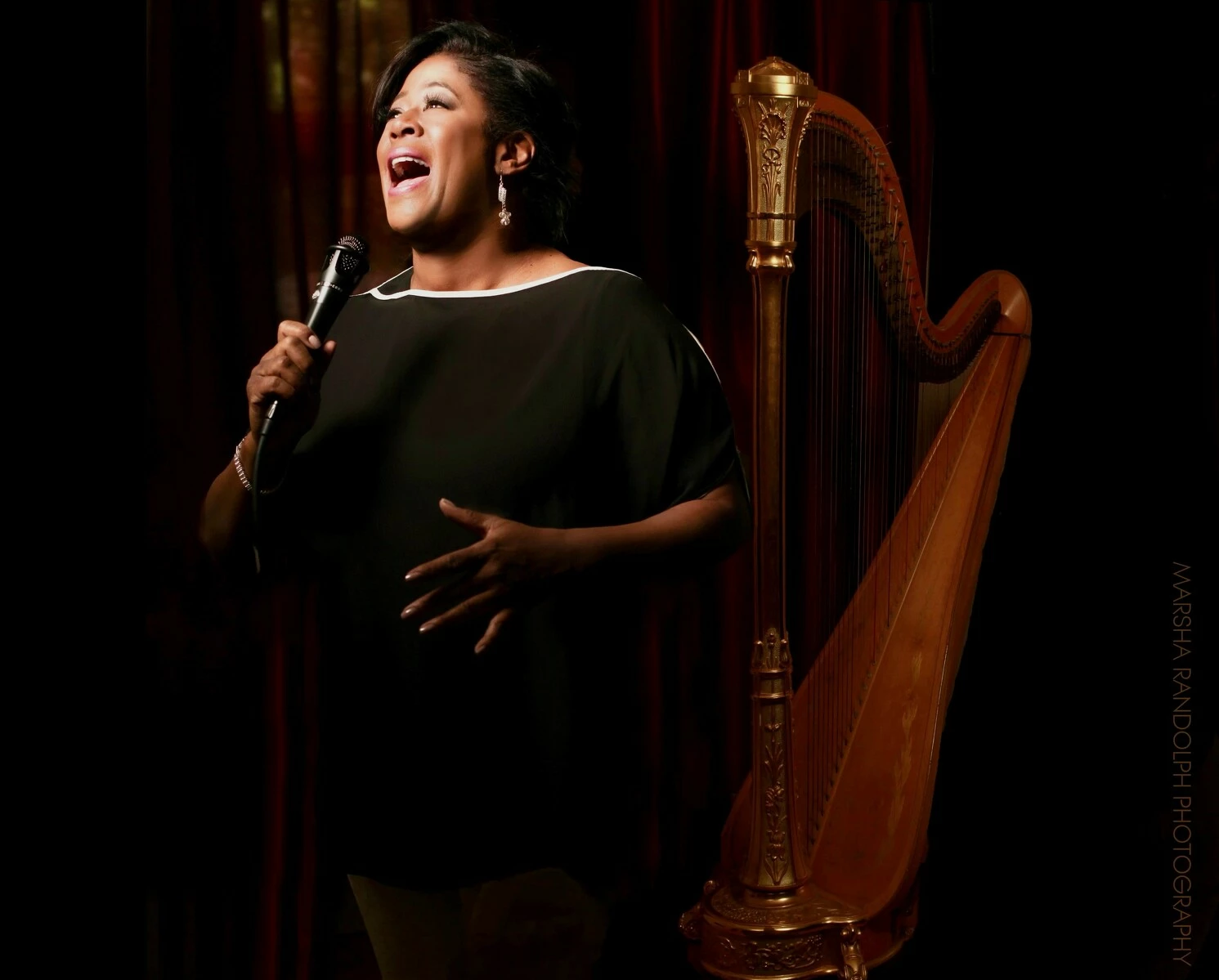 A woman sings into a microphone in front of a harp.