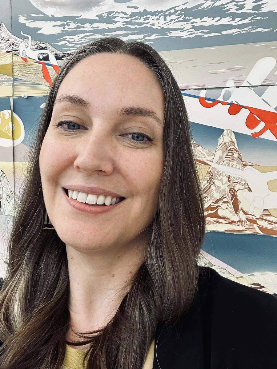 Selfie-like portrait of a woman with dark brown hair posing in front of a large artwork.