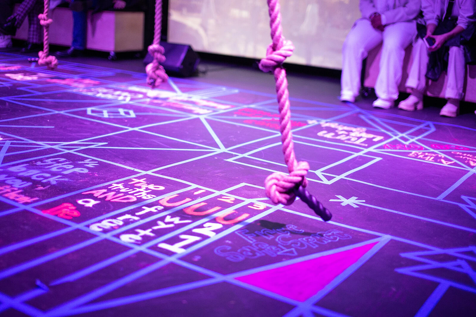 A thick rope with notes hangs above a purple-lit floor covered in diagrams.