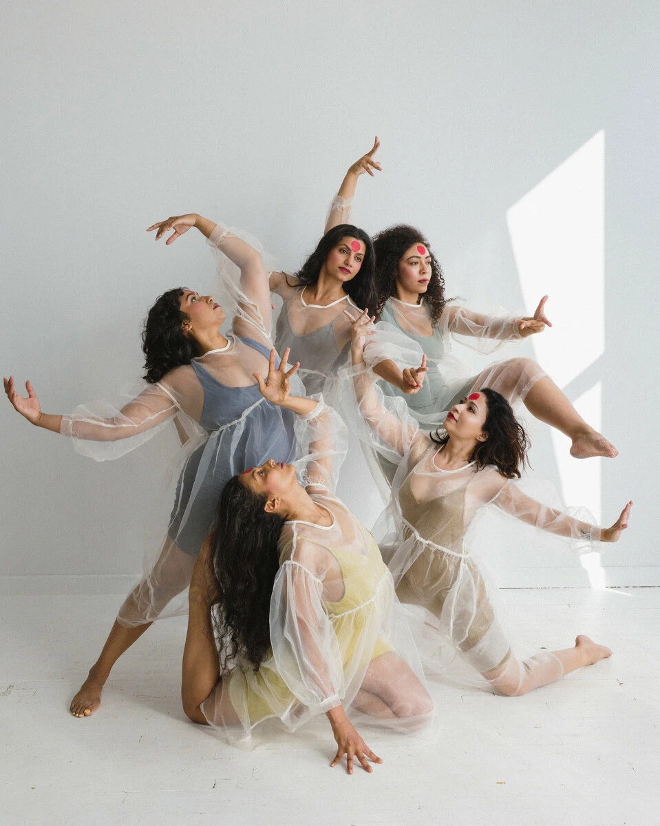 Five people in transparent dresses dance moving their arms and legs.