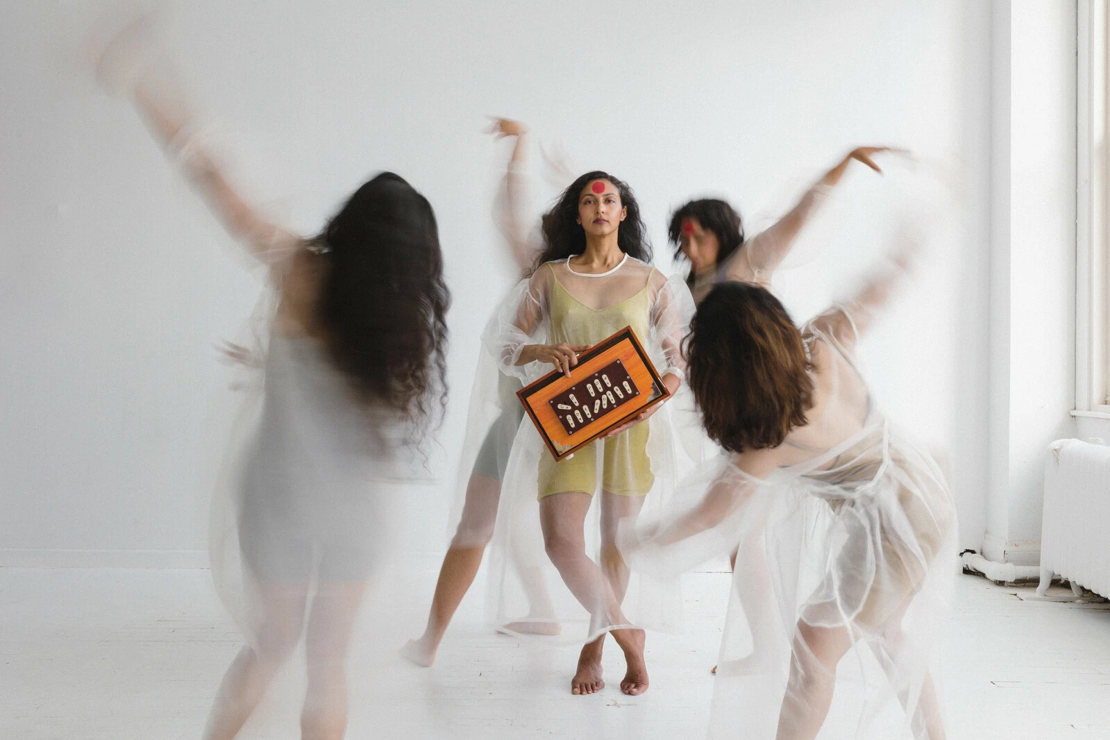 Four people in transparent dresses circle around one person in the center.