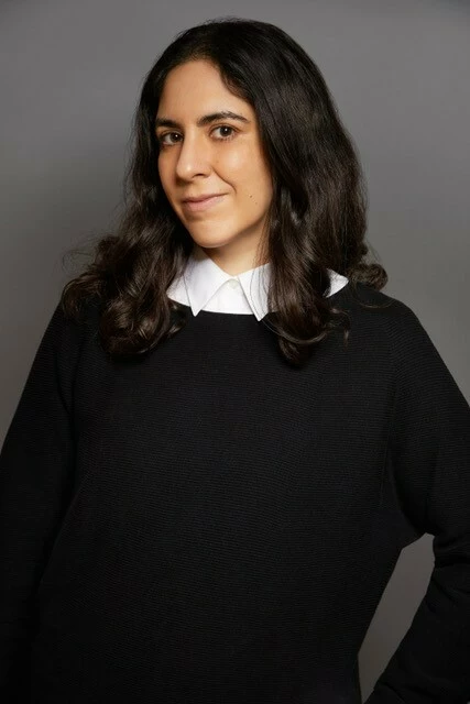 Portrait of a female-presenting person in a black shawl against a grey backdrop