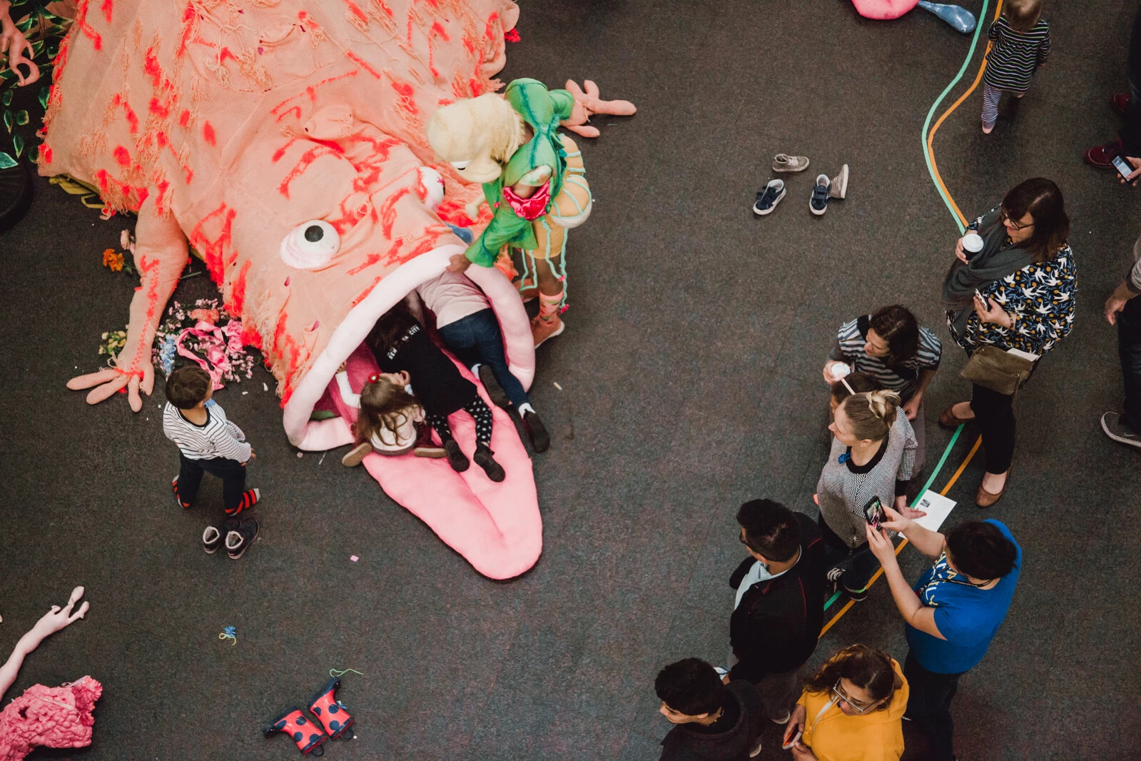 A group gathers near a large pink monster that has a few pairs of legs hanging out of its mouth