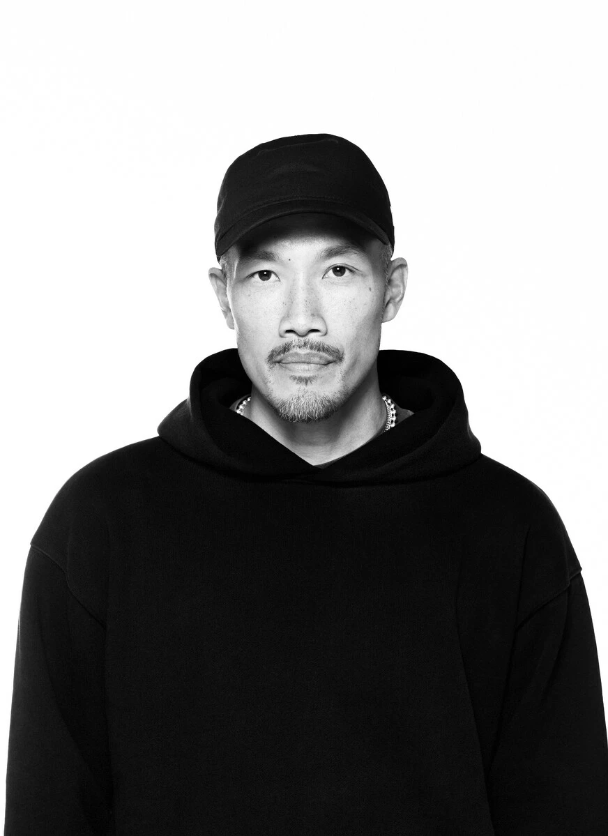 Black and white portrait of a man in a black hat and hoodie against a stark white background