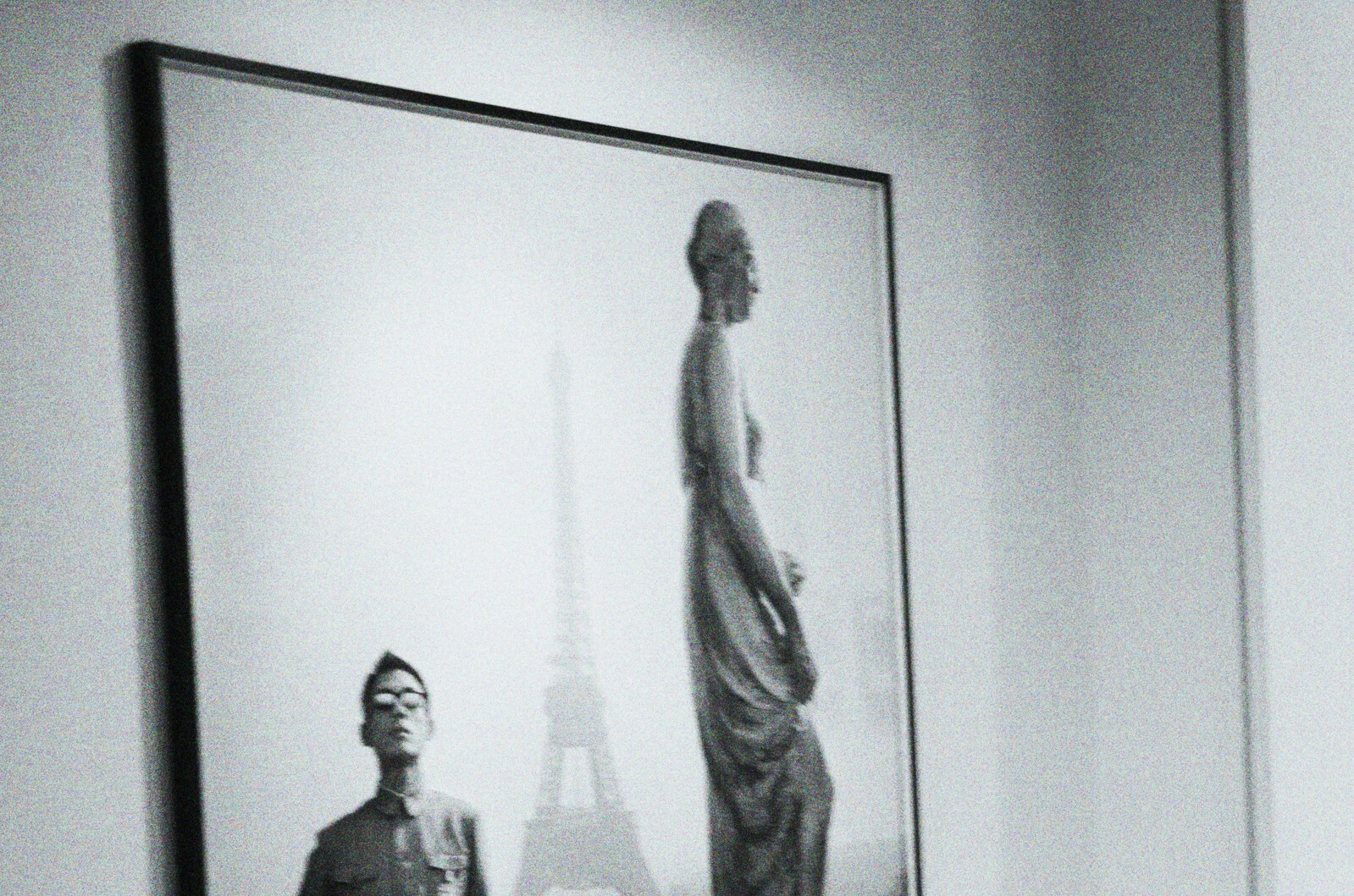 Greyscale image of the top half of a framed image of a sculpture and a person with the Eiffel Tower a hazy object in the background