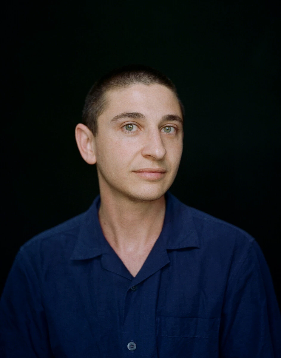 Three-quarter portrait of a person with a shaved head against a black background