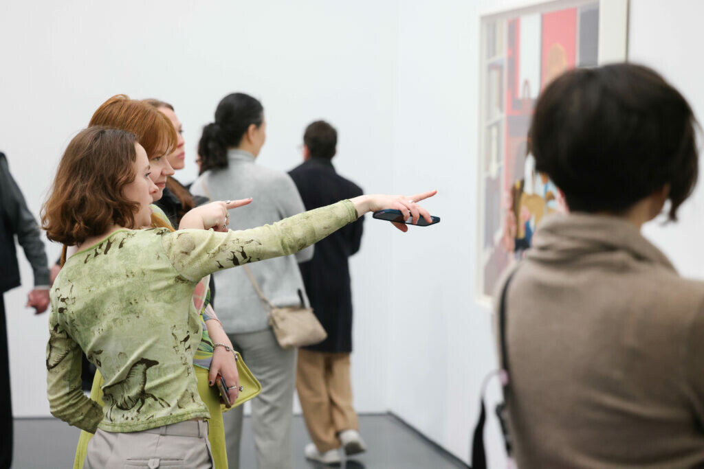 Several people in a gallery space. One person points to a painting on the wall.