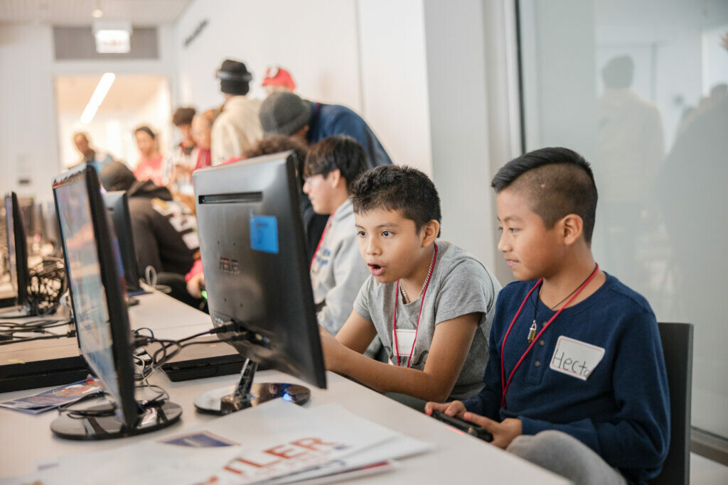 Two kids sit immersed in a computer screen, one with mouth agape