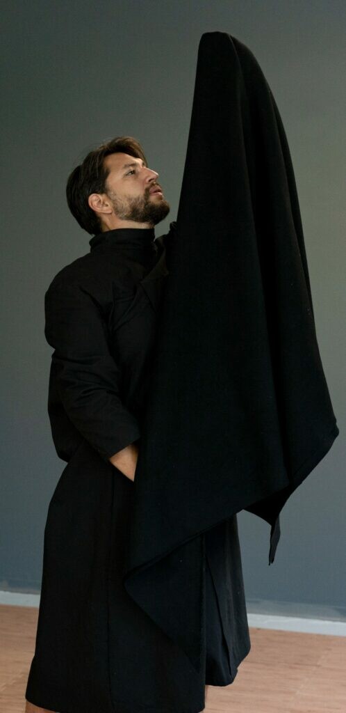 A man dressed in black holds a large black fabric up above his head