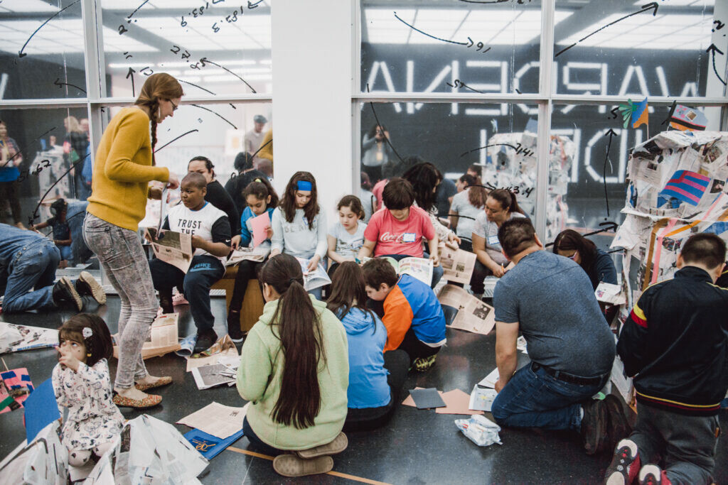 Niños y adultos se sientan en el suelo con materiales para hacer arte.