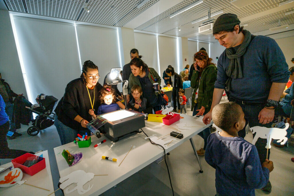 Kids and adults gather in a darkened room around a projector